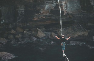 a man balancing on a tightrope between cliffs. 