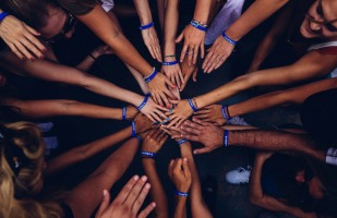numerous people with their hands together in a huddle.