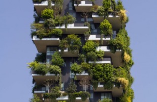 an apartment building with plants and trees sprawling from it's balconies.