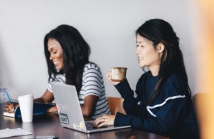 two women having coffee and working on their laptops.