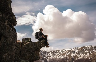 Man sitting on a mountain ledge overlooking a valley